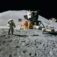 A public domain photo of Apollo 15 on the Moon's surface, with the flag flying and a saluting astronaut. The Moon Lander and Moon Rover to the right.